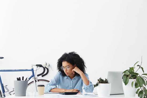 Retrato horizontal de uma empresária séria de pele escura isolada sobre o interior do escritório