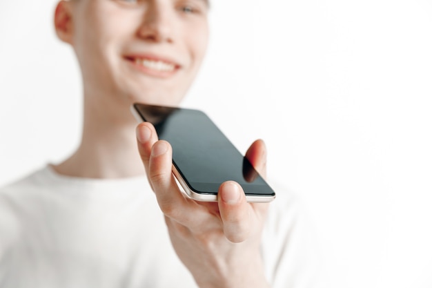 Retrato interior de um jovem atraente isolado em um fundo cinza, segurando o smartphone, usando o controle de voz, sentindo-se feliz e surpreso. Emoções humanas, conceito de expressão facial.