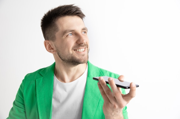 Retrato interno de jovem atraente isolado em um espaço cinza, segurando um smartphone, usando o controle de voz, sentindo-se feliz e surpreso