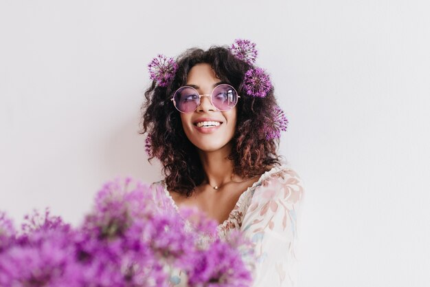 Retrato interno de uma garota negra despreocupada, olhando para longe durante a sessão de fotos com flores. Mulher africana satisfeita, expressando interesse enquanto posava com alliums.