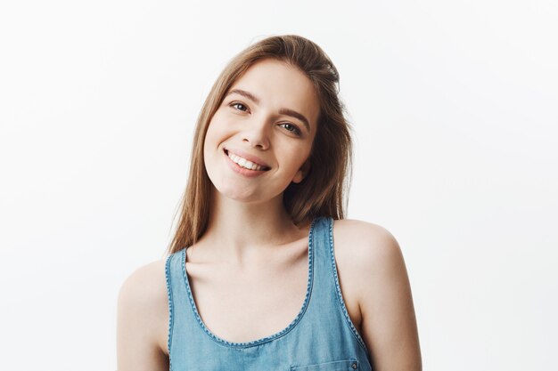 Retrato isolado da menina alegre atraente jovem estudante com cabelos escuros e olhos castanhos, vestindo camisa azul casual, sorrindo com prazer e expressão do rosto relaxado.