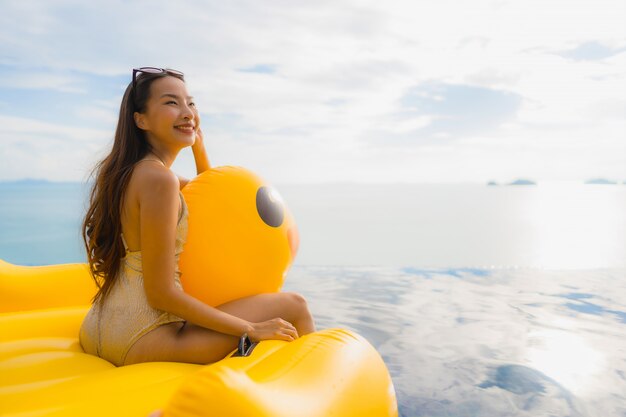 Retrato, jovem, mulher asian, ligado, inflável, flutuador, pato amarelo, ao redor, piscina ao ar livre, em, hotel, e, recurso