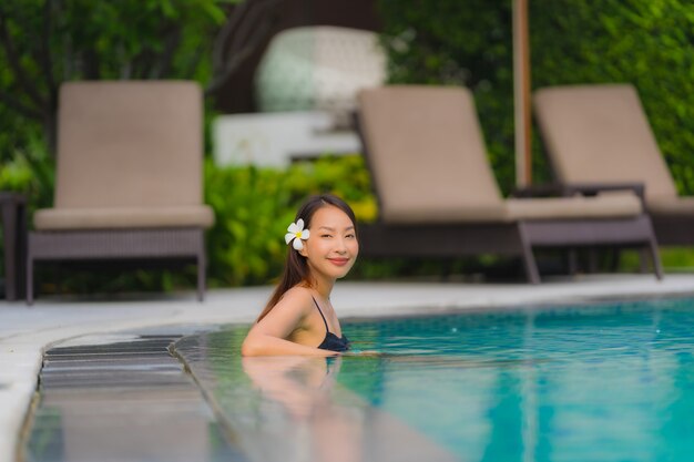 Retrato, jovem, mulher asian, relaxe, sorrizo, feliz, ao redor, piscina exterior, em, hotel, recurso, com, mar, oceânicos, vista