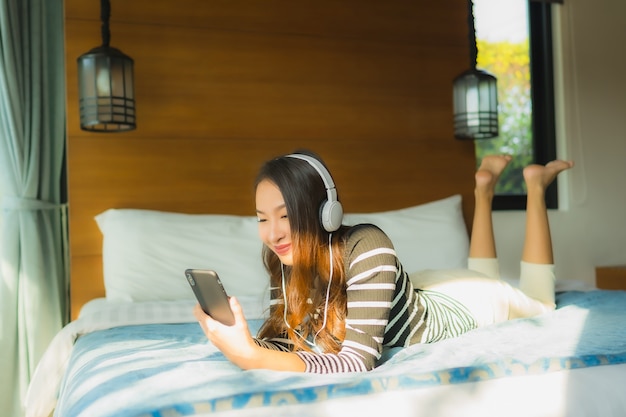 Retrato jovem mulher asiática usando telefone celular inteligente com fone de ouvido para ouvir música no quarto