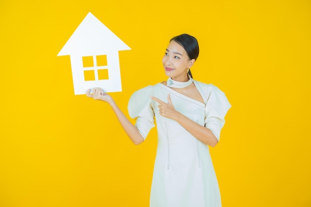 Retrato linda jovem asiática com casa ou sinal de papel em casa na cor de fundo.