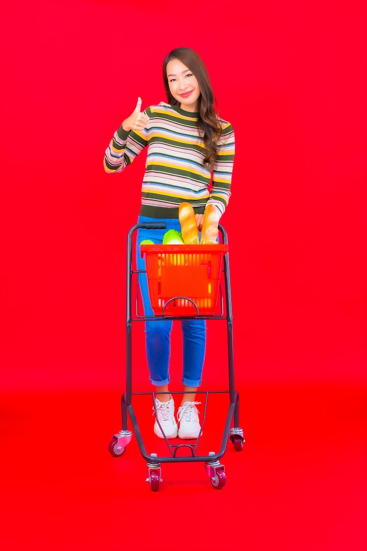 Foto grátis retrato linda jovem asiática com cesta de supermercado na parede vermelha isolada