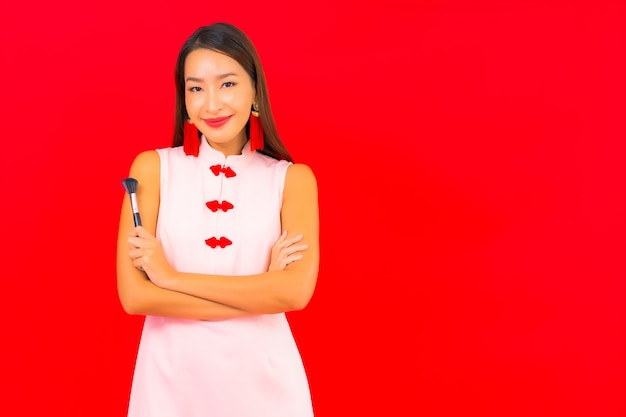 Retrato linda jovem asiática com escova cosmética de maquiagem na parede vermelha isolada