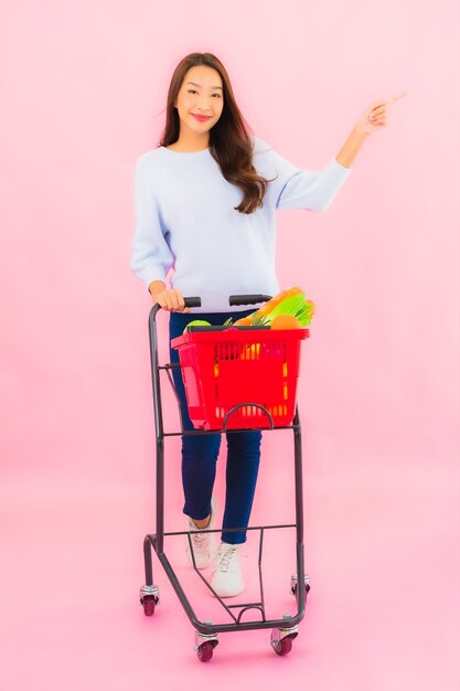 Retrato linda jovem asiática com frutas, vegetais e mercearia em uma cesta na parede rosa isolada