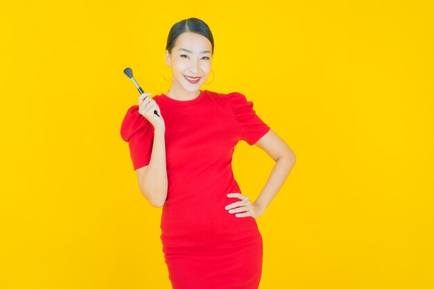 Retrato linda jovem asiática com maquiagem escova cosmética em amarelo
