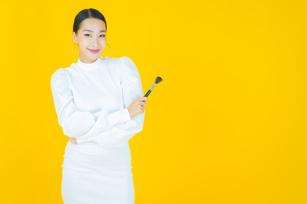 Retrato linda jovem asiática com maquiagem escova cosmética em amarelo