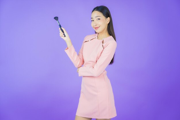 Retrato linda jovem asiática com pincel de maquiagem cosmético sobre fundo colorido
