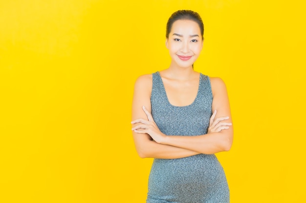 Retrato linda jovem asiática com roupa esportiva pronta para se exercitar na parede amarela.