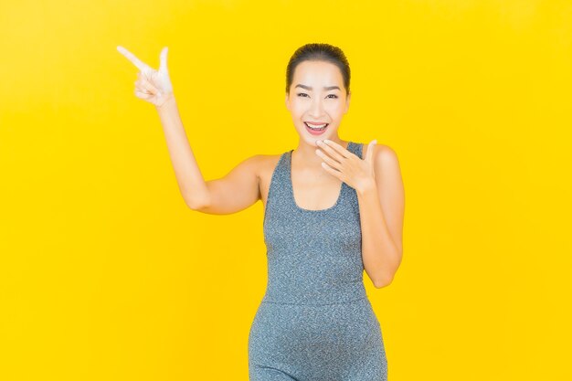 Retrato linda jovem asiática com roupa esportiva pronta para se exercitar na parede amarela.