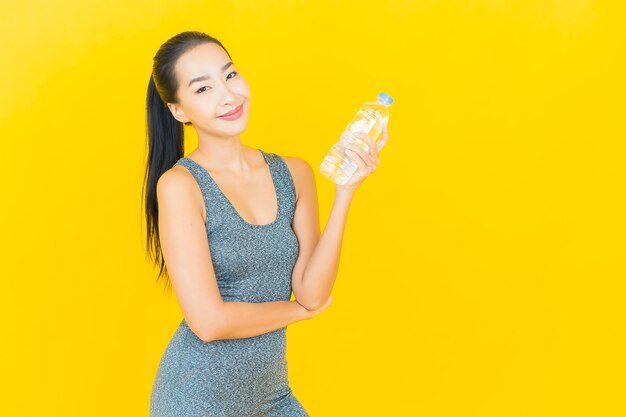 Retrato linda jovem asiática com roupas esportivas e garrafa de água na parede amarela