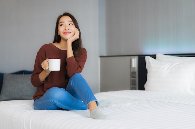 Retrato linda jovem asiática com xícara de café na cama, no interior do quarto