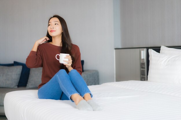 Retrato linda jovem asiática com xícara de café na cama, no interior do quarto