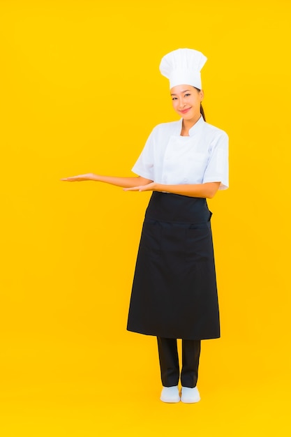 Foto grátis retrato linda jovem asiática no chef ou cozinheiro uniforme com chapéu amarelo isolado.