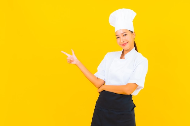 Retrato linda jovem asiática no chef ou cozinheiro uniforme com chapéu amarelo isolado.