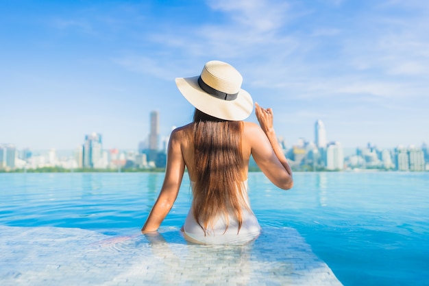 Retrato linda jovem asiática relaxando ao redor da piscina ao ar livre com vista da cidade