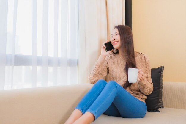 Retrato linda jovem asiática relaxando sorriso feliz com telefone inteligente com café no sofá