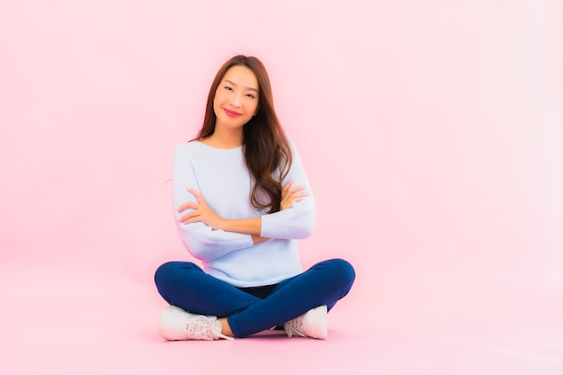 Retrato linda jovem asiática sentada no chão com uma parede de cor rosa isolada