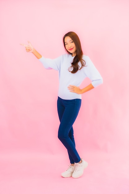 Foto grátis retrato linda jovem asiática sorrindo com ação na parede rosa isolada