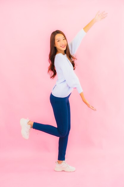 Retrato linda jovem asiática sorrindo com ação na parede rosa isolada