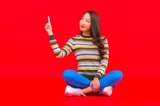 Retrato linda jovem asiática sorrindo com ação na parede vermelha isolada