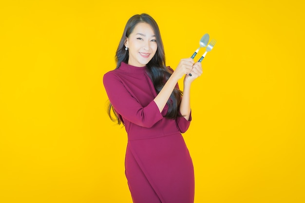 Retrato linda jovem asiática sorrindo com colher e garfo amarelo