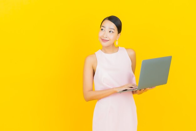 Retrato linda jovem asiática sorrindo com computador laptop em amarelo