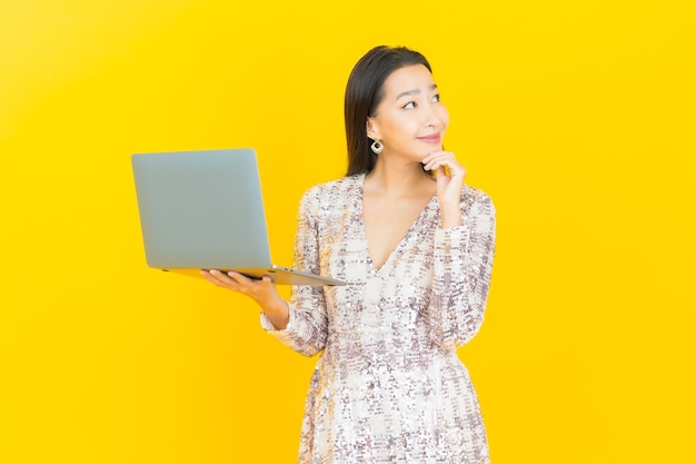 Retrato linda jovem asiática sorrindo com computador laptop em amarelo