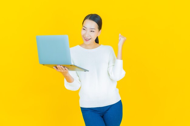 Retrato linda jovem asiática sorrindo com computador laptop em amarelo