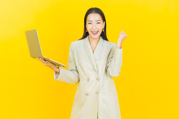 Retrato linda jovem asiática sorrindo com computador laptop na parede isolada