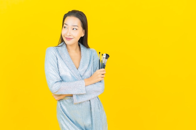 Retrato linda jovem asiática sorrindo com pincel de maquiagem cosmética na parede amarela