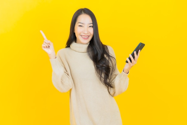 Retrato linda jovem asiática sorrindo com smartphone na parede amarela