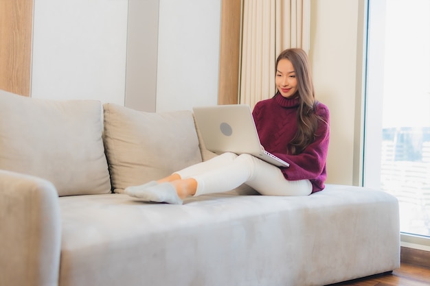 Retrato linda jovem asiática usando computador laptop no sofá no interior da sala de estar