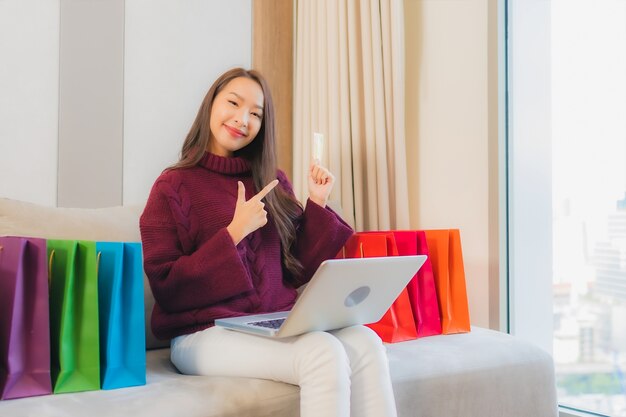 Retrato linda jovem asiática usando computador portátil com cartão de crédito para fazer compras online no sofá