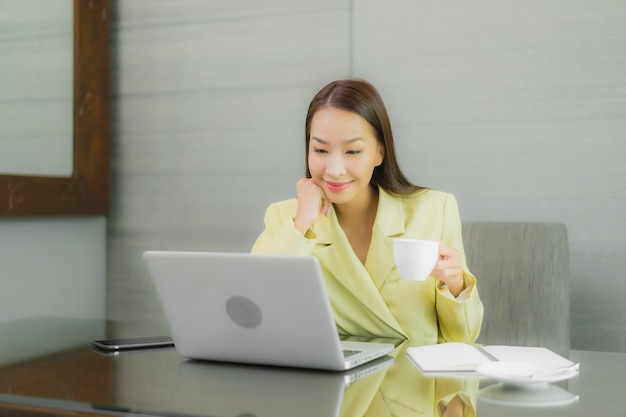 Retrato linda jovem asiática usando computador portátil com celular inteligente na mesa de trabalho na sala interior