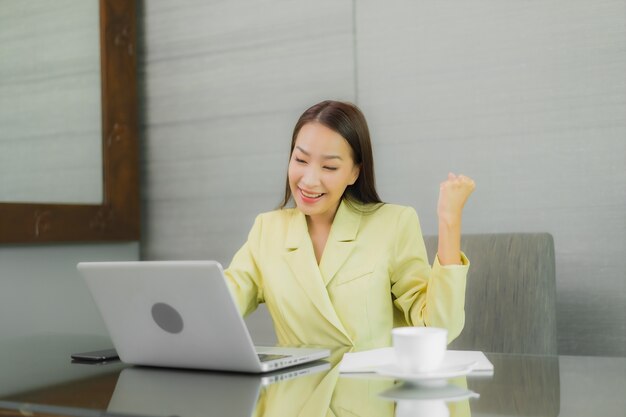 Retrato linda jovem asiática usando computador portátil com celular inteligente na mesa de trabalho na sala interior