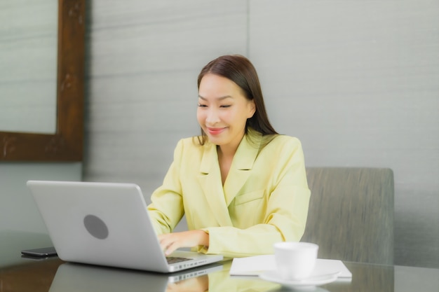 Retrato linda jovem asiática usando computador portátil com celular inteligente na mesa de trabalho na sala interior