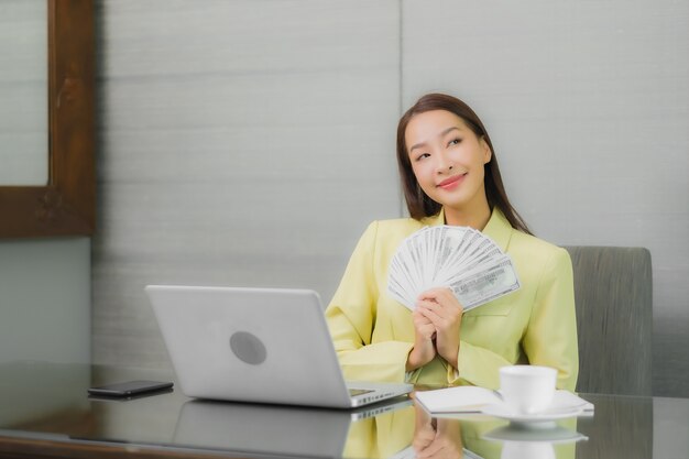 Retrato linda jovem asiática usando computador portátil com celular inteligente na mesa de trabalho na sala interior