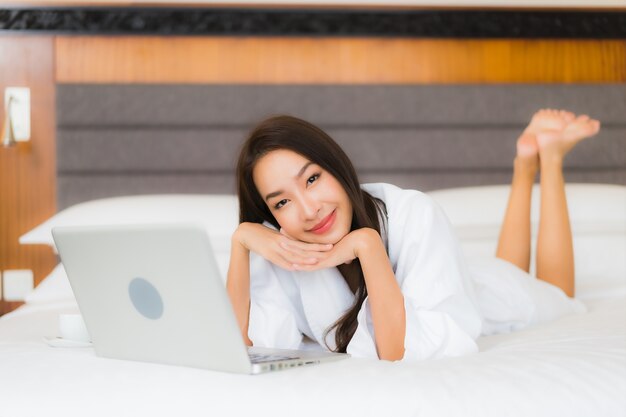 Retrato linda jovem asiática usando laptop na cama no interior do quarto