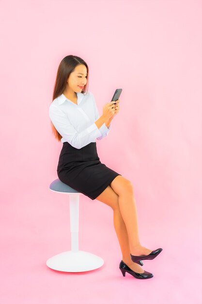 Retrato linda jovem asiática usando telefone celular inteligente na parede rosa isolada