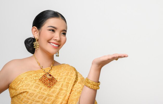 Retrato Linda mulher asiática em traje tradicional de vestido tailandês sorri e pose com a palma da mão aberta com graciosamente na parede branca