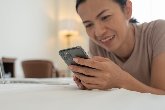 Retrato matinal de uma mulher asiática bonita sorridente usando um smartphone