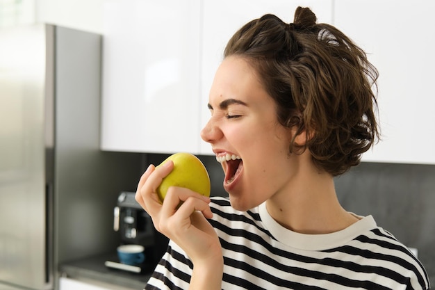 Foto grátis retrato próximo de mulher sorridente na cozinha segurando uma maçã comendo frutas tendo um saudável