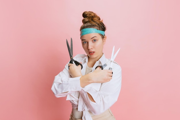 Retrato recortado de jovem costureira com uma tesoura posando isolado sobre o fundo rosa do estúdio