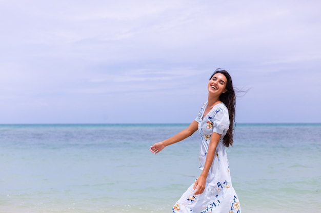 Retrato romântico de mulher com vestido longo azul na praia à beira-mar em dia de vento