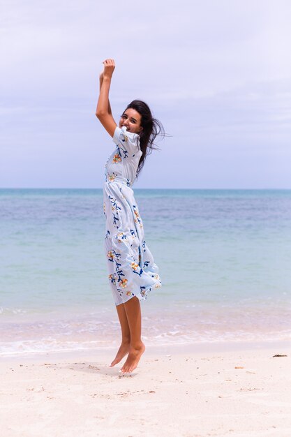 Retrato romântico de mulher com vestido longo azul na praia à beira-mar em dia de vento
