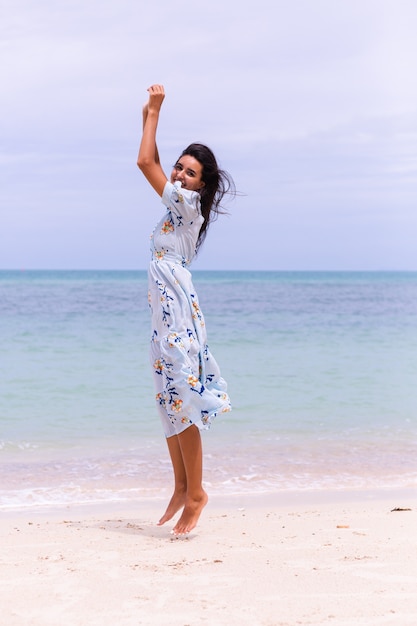 Retrato romântico de mulher com vestido longo azul na praia à beira-mar em dia de vento